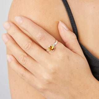 Close-up of a hand wearing a silver ring with a yellow gemstone on a neutral background