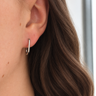 A close-up of a woman's ear wearing a small, polished silver hoop earring.
