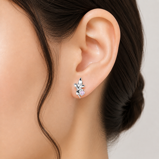 A close-up of a model's ear wearing a silver-toned leaf-shaped stud earring with a small clear crystal and a tiny pale pink accent stone, against a light neutral background.