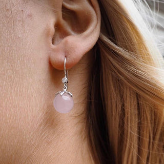 Close-up of an ear wearing a pink gemstone earring with a silver setting.