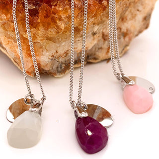 Three necklaces with teardrop-shaped gemstones against a stone background