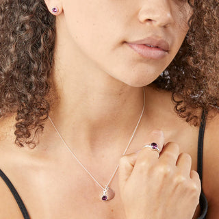 Close-up of a woman wearing a silver necklace with a purple gemstone, matching earrings, and ring.