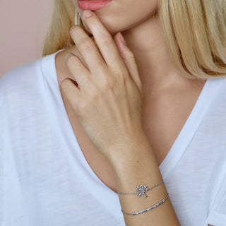Close-up of a woman's hand wearing a silver bracelet with a tree charm on a plain background