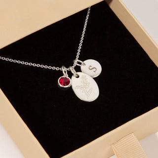 Silver necklace with engraved charms and a red gemstone in a box