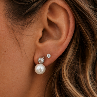 Close-up of an ear wearing a pearl earring with a small diamond, against a blurred background.