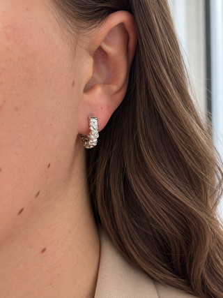 A close-up of a woman's ear wearing a small silver huggie hoop earring with textured, organic-shaped crystal details.