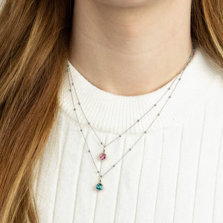 Necklace with colorful pendants worn by a person with long hair, wearing a white sweater.
