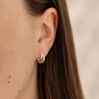 Close-up of an ear wearing a gold hoop earring with a blurred background