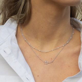 Close-up of a person wearing a silver necklace with a small pendant on a plain background