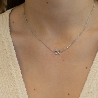 Silver necklace with a small couple pendant on a person wearing a beige sweater.