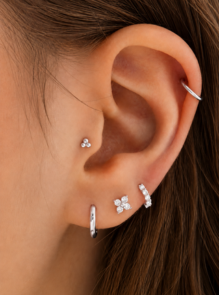 Close-up of a person's ear showcasing multiple silver ear piercings, including a hoop in the lobe, a small stud, a floral cluster, a curved barbell, and a piercing in the helix.