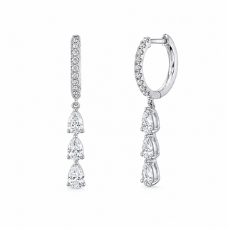 A pair of silver huggie hoop earrings with a vertical bar studded with small clear stones and three pear-cut dangling stones, shown on a plain white background.