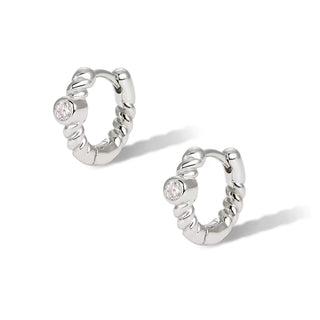 A pair of silver huggie hoop earrings with a textured, twisted outer edge and a small clear round gemstone set on the front, shown on a white background with soft shadows.