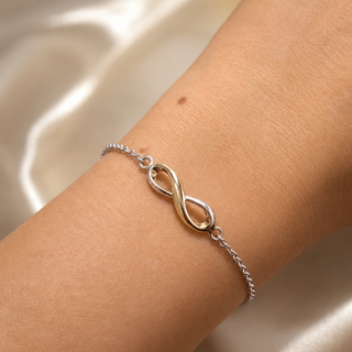 Silver bracelet with an infinity symbol on a wrist against a satin background