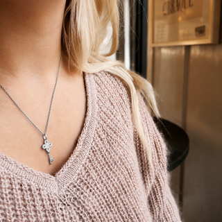 Person wearing a pink knit sweater with a silver necklace featuring a cross pendant.