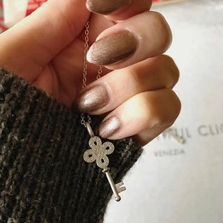 Hand holding a necklace with a key-shaped pendant against a blurred background