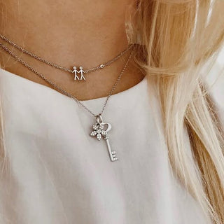 Close-up of a person wearing two necklaces with key and couple pendants on a white background.