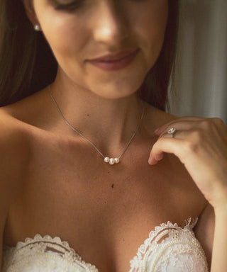 Close-up of a woman wearing a pearl necklace and ring, with a soft focus on her face.