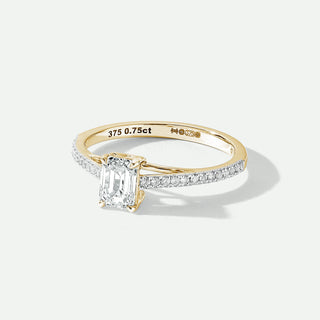 Gold ring with emerald-cut diamond and pave set diamonds on a white background