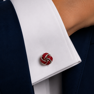 Red and silver cufflink on a white shirt cuff with a navy suit jacket.