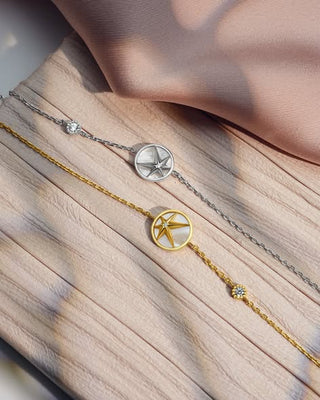 Two gold and silver bracelets with star-shaped charms on a soft fabric background