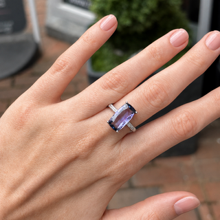 Hand wearing a ring with a purple gemstone on a blurred background