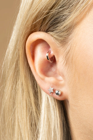 Close-up of an ear with three earrings: a star, a circle, and a smaller star.