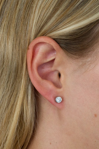 Close-up of an ear wearing a diamond stud earring with blonde hair.