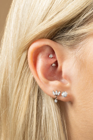 Close-up of an ear with multiple diamond earrings on a neutral background