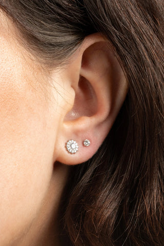 Close-up of an ear wearing two diamond stud earrings with a blurred background.