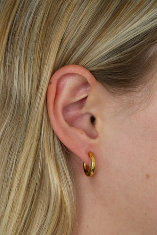 Close-up of a person wearing a gold hoop earring with blonde hair.