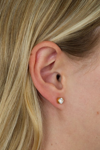 Close-up of an ear wearing a gold earring with a clear gemstone.