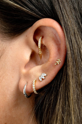 Close-up of an ear with multiple gold and platinum plated titanium earrings.
