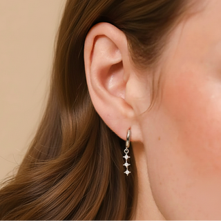 Close-up of a person wearing a silver earring with star-shaped charms on a beige background