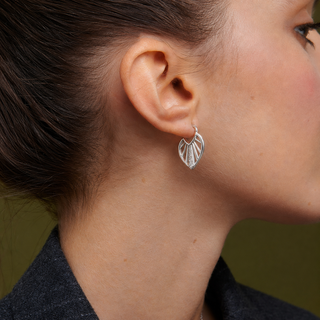 Close-up of a person wearing silver leaf-shaped earrings with a blurred background