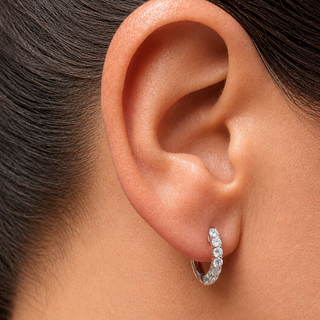 A close-up of a person's ear wearing a small white gold huggie hoop earring set with diamonds stones.
