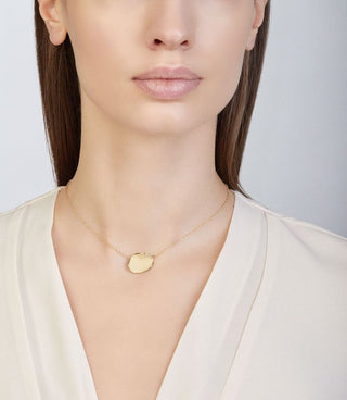 Woman wearing a gold necklace with a heart pendant against a neutral background
