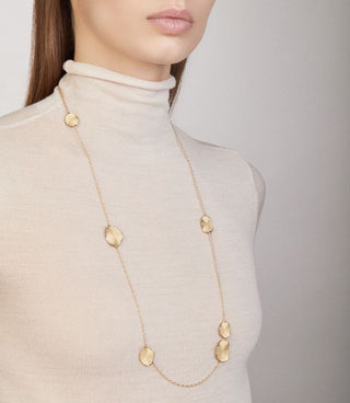 Gold necklace worn by a person in a beige turtleneck against a neutral background